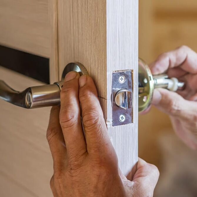 Hands fitting a new door handle and latch into the edge of a wooden door